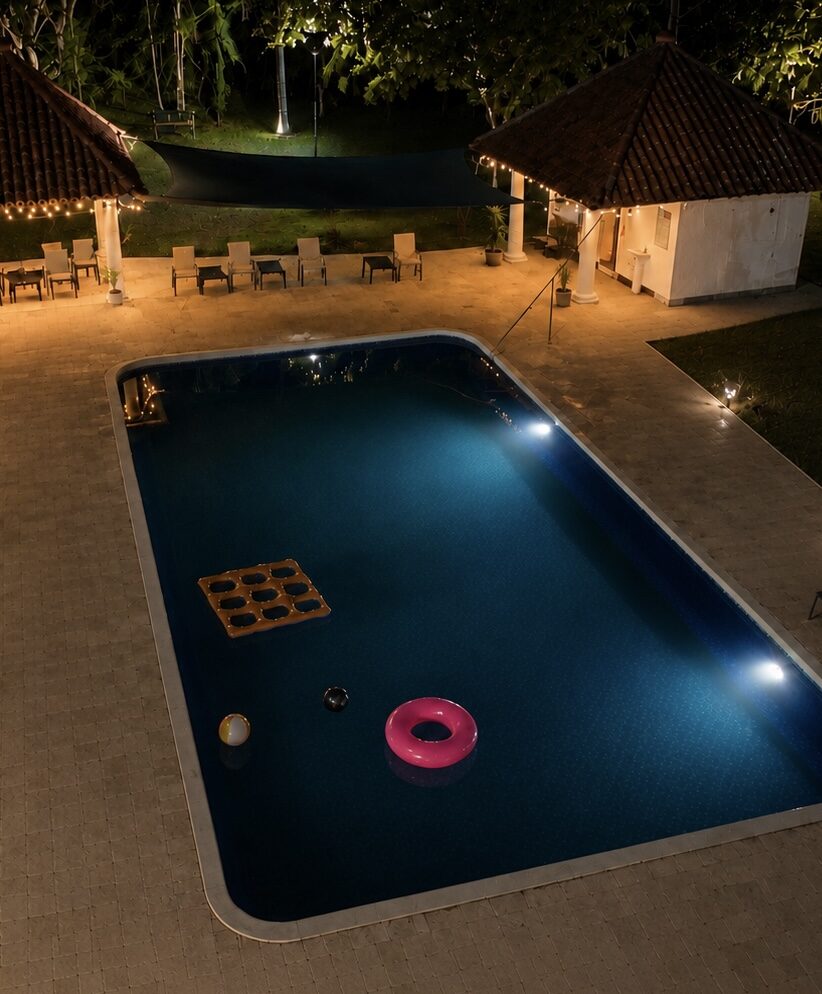 La piscina iluminada de noche, rodeada de terrazas y sillas de descanso