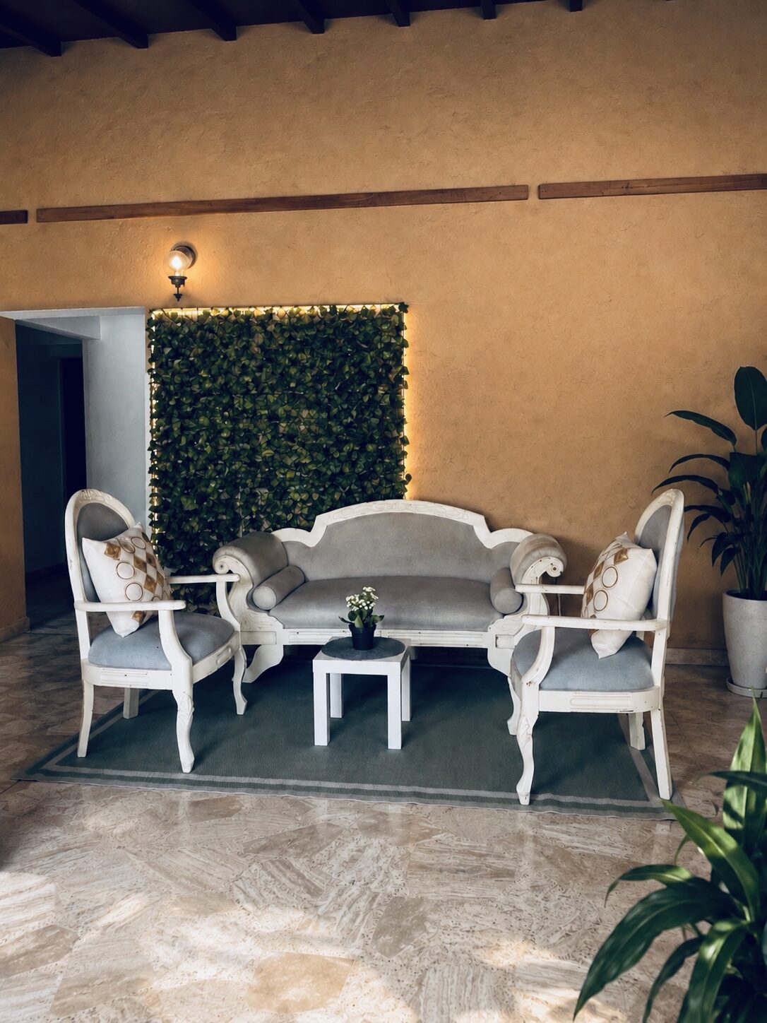 Zona de estar con muro verde, sillones blancos y plantas